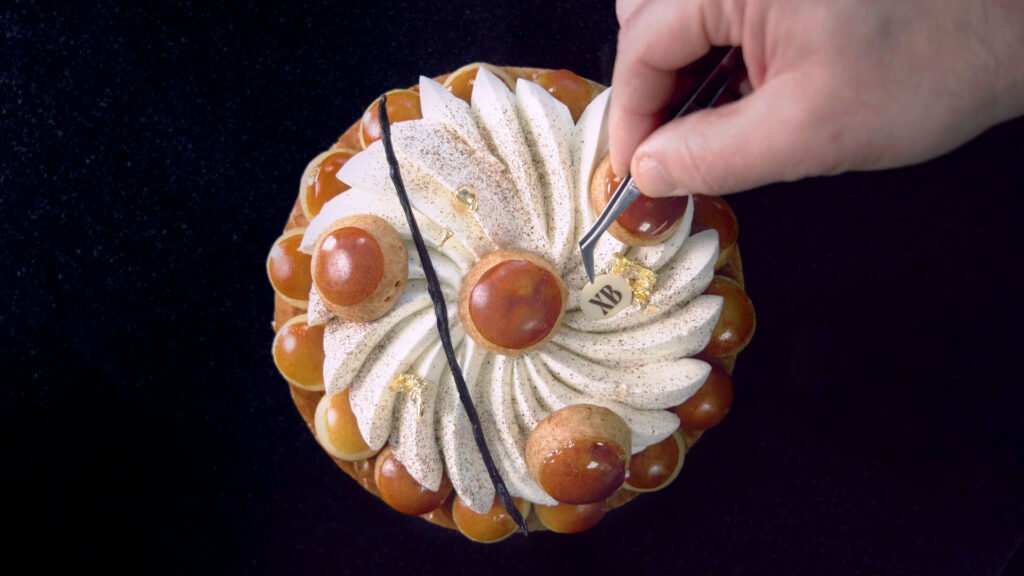 Main de pâtissier apportant la touche finale à son dessert.